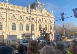 Przewodnik oprowadza dzieci podczas wycieczki przed Pałacem Poznańskiego w Łodzi