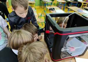 Uczniowie klasy 2c obserwują pracę drukarki 3D, która wykonuje bombki