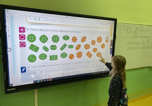 Uczennica wykonuje ćwiczenia - kolorowanie guzików przy tablicy interaktywnej