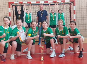 Trener z uczniami stoi przy bramce na sali gminastycznej