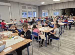 Dzieci sziedzą przy stolikach na warszyaych plastycznych