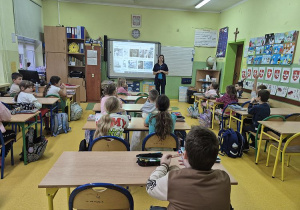 Uczniowie siedzą przy stolikach słuchają prelekcji o zawodzie pielęgniarki