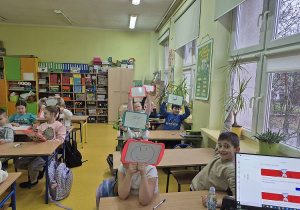 Uczniowie pokazuja uśmiechnięte buzie narysowane na biłaych tabliczkach